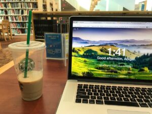 A laptop is open on a library table. On it, the google extension momentum is open. Next to it is a half-drunk starbucks drink. 
